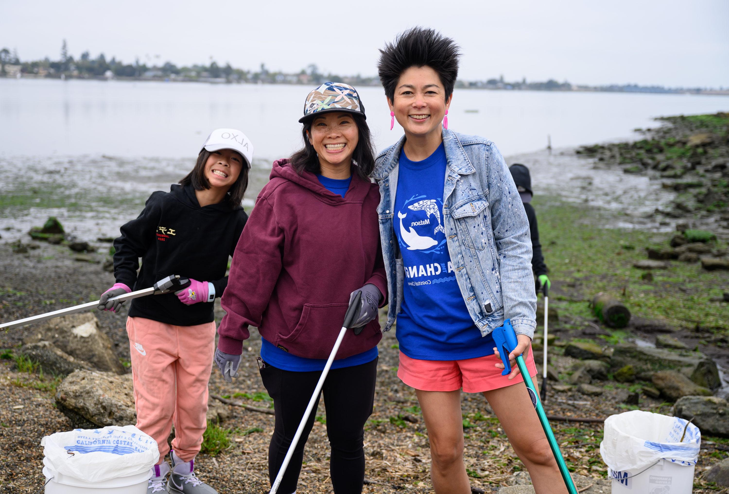 Volunteers pose with buckets and grabbers with the Oakland Estuary in the background. 